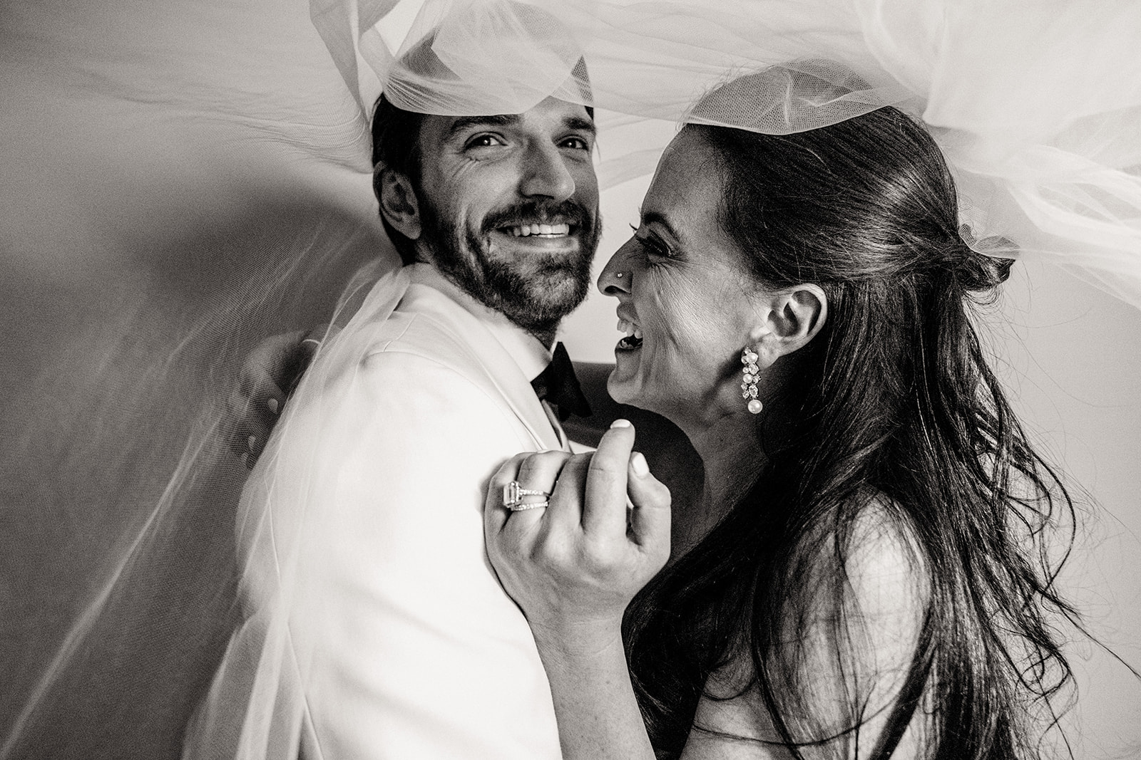 black and white candid photo of a husband and wife couple laughing under the bride's veil