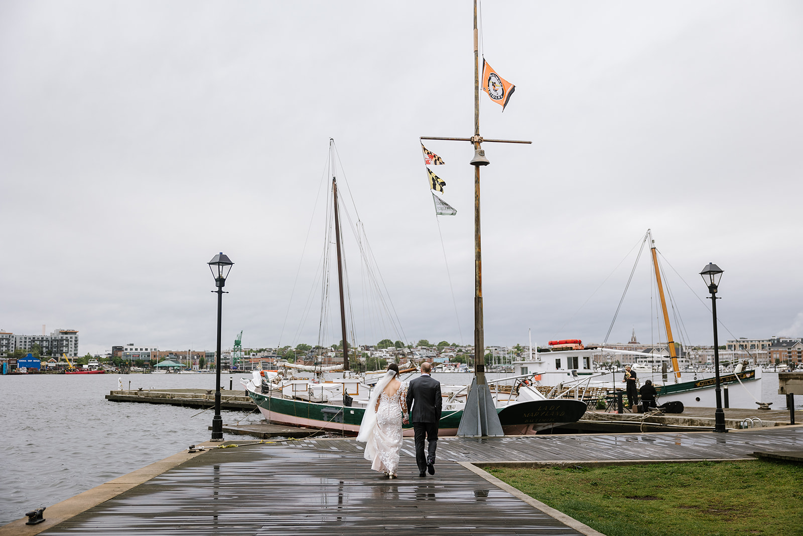 bride and groom walking along pier at frederick douglass maritime park wedding venue with sailboats behind them