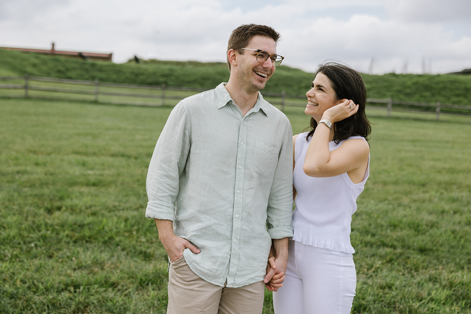 engaged couple standing next to each other laughing at fort mchenry in the summer