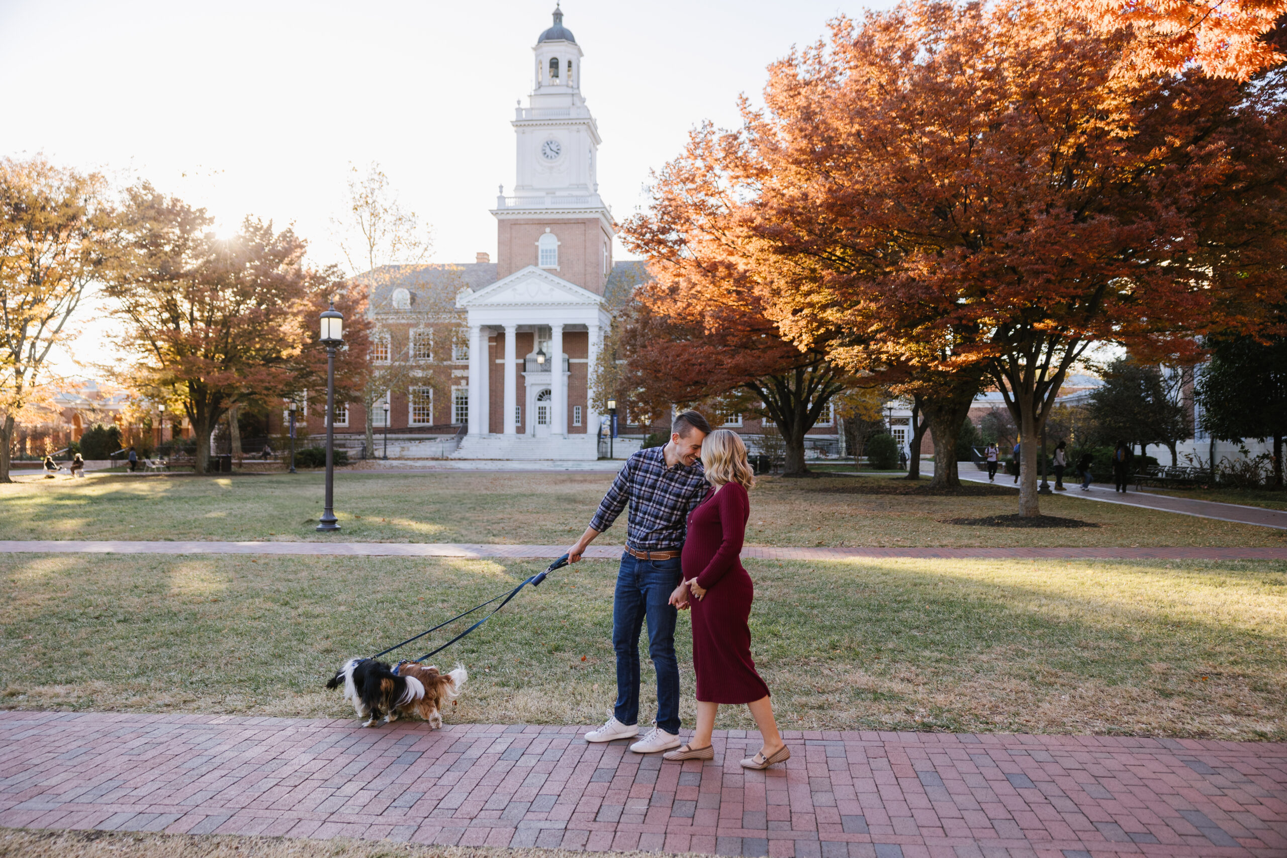 engaged couple walking with their dogs on johns hopkins homewood campus at sunset in the fall