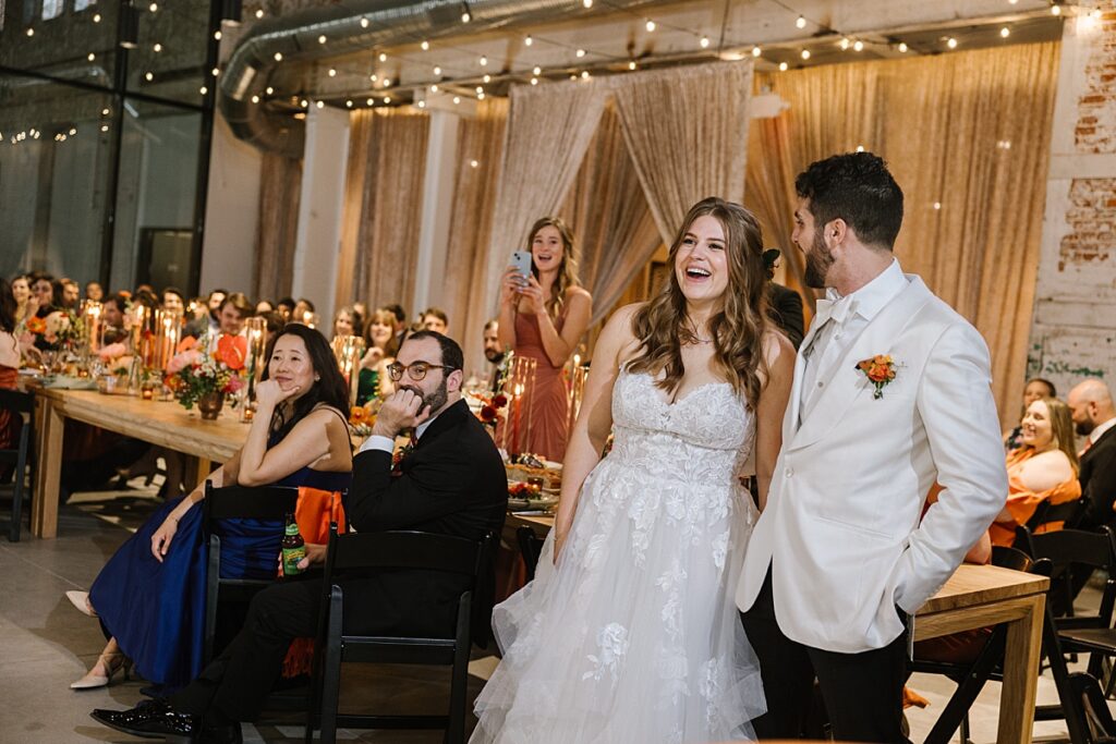 a couple stands in front of wedding reception table at the butterfly room laughing during a speech