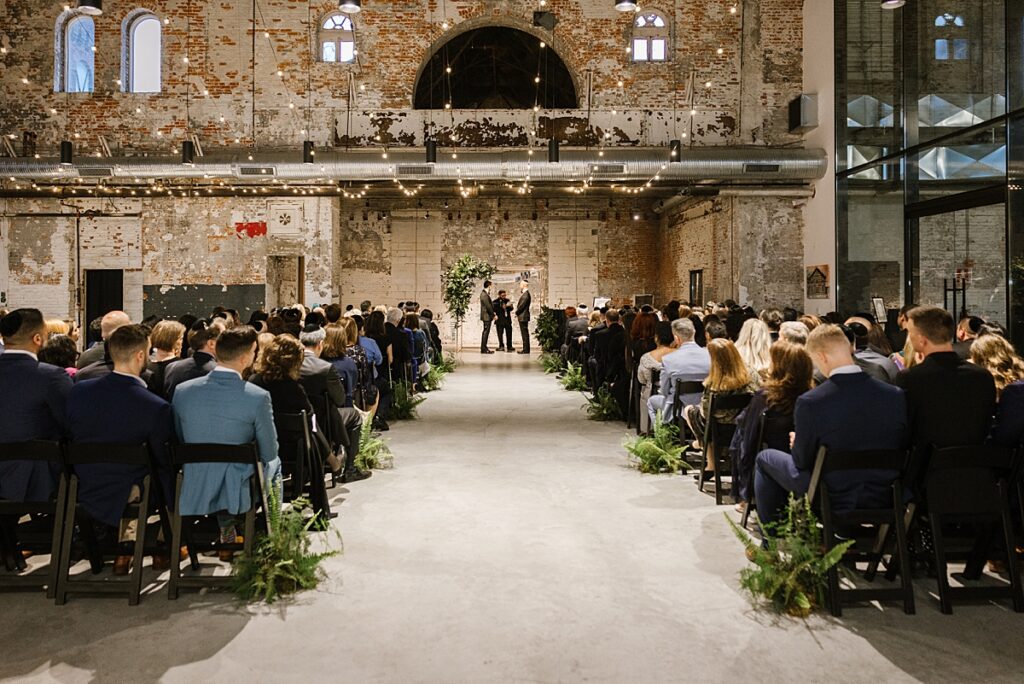 gay couple is married under a chuppah at the butterfly room, an industrial venue with a moody, darker vibe