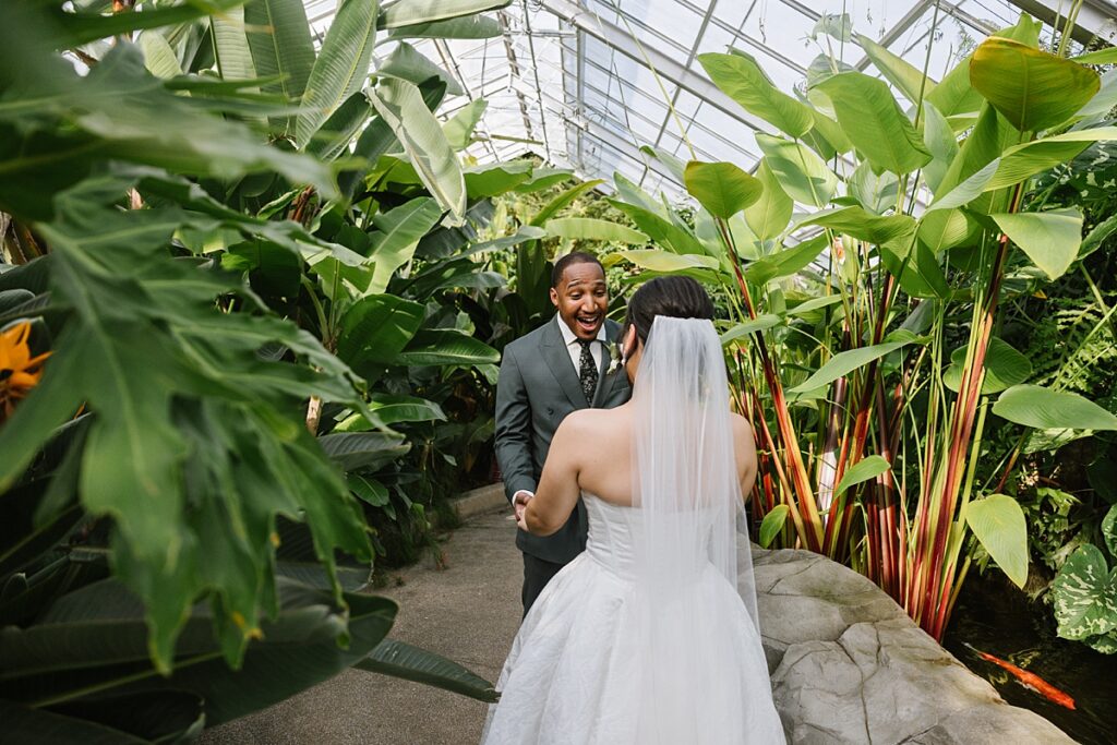 black couple embraces as groom sees bride for first time among plants an intimate wedding at rawlings conservatory