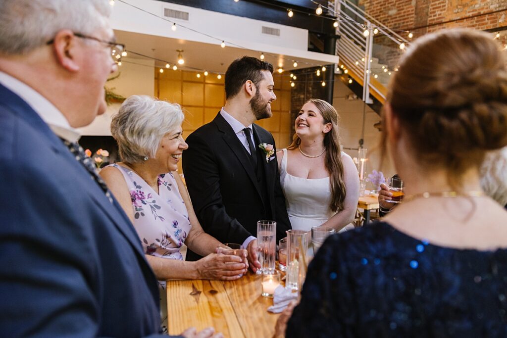 bride and groom enjoy a joyful moment standing near parents during wedding cocktail hour at woodberry kitchen